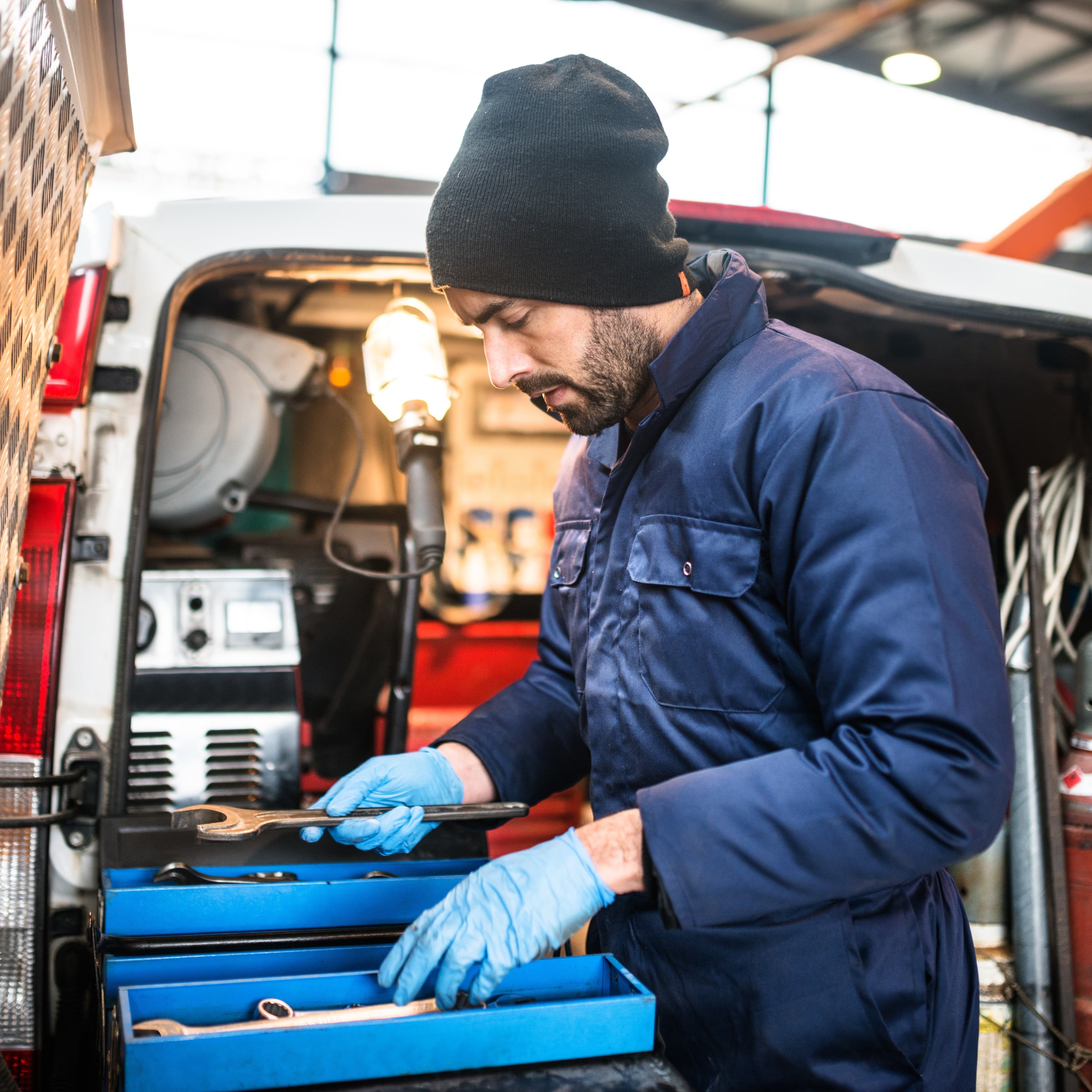 Fleet maintenance technician working from a mobile service van, checking tools during vehicle repair. Fleet maintenance technician working from a mobile service van, checking tools during vehicle repair.