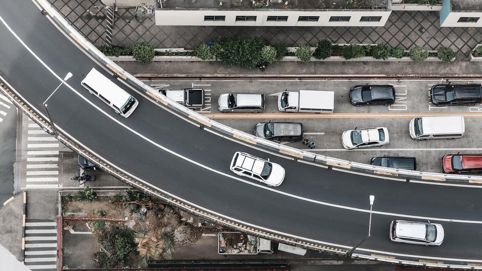 Aerial view of vehicles traveling and parked along a curved urban roadway. Aerial view of vehicles traveling and parked along a curved urban roadway.