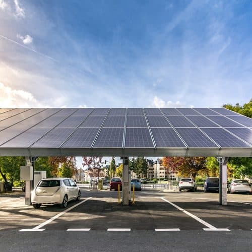Solar panel canopy installed over a parking lot, shading parked cars and supporting electric vehicle charging infrastructure beneath a clear blue sky. Solar panel canopy installed over a parking lot, shading parked cars and supporting electric vehicle charging infrastructure beneath a clear blue sky.