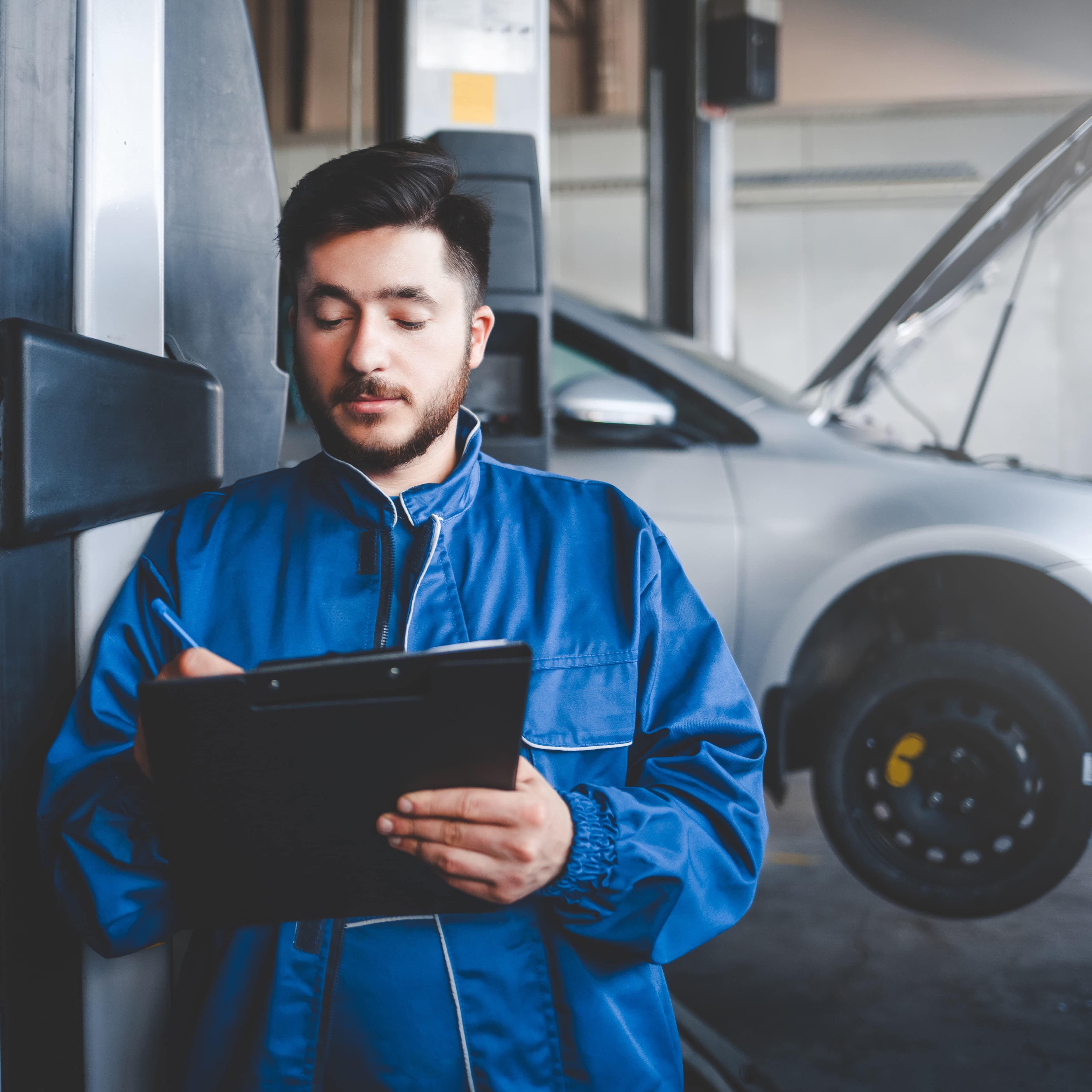 Fleet maintenance technician using a tablet to inspect a vehicle in an automotive service center. Fleet maintenance technician using a tablet to inspect a vehicle in an automotive service center.