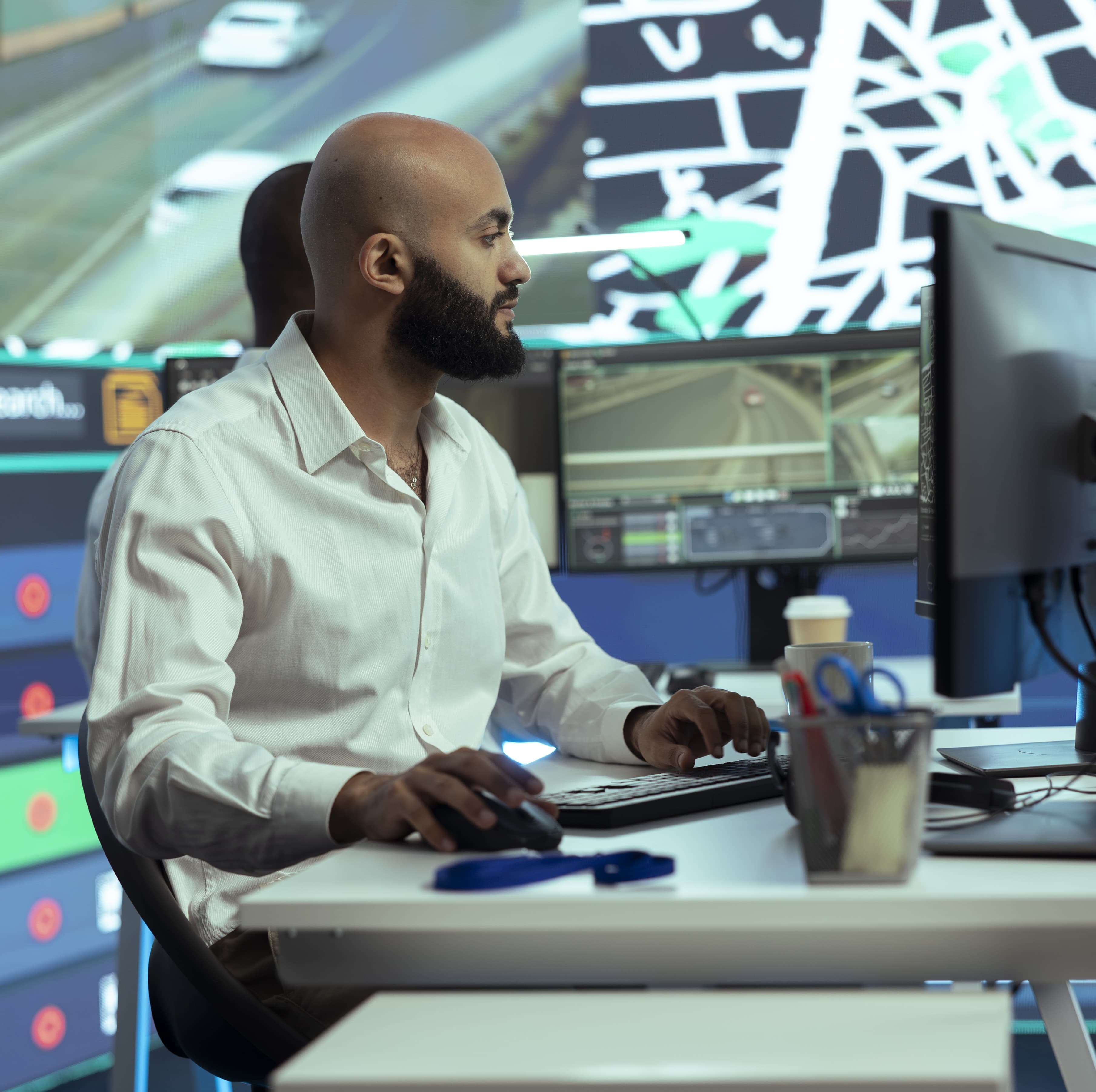 A man working at a computer in a control room monitoring traffic and vehicle data on multiple screens as part of fleet management operations. A man working at a computer in a control room monitoring traffic and vehicle data on multiple screens as part of fleet management operations.