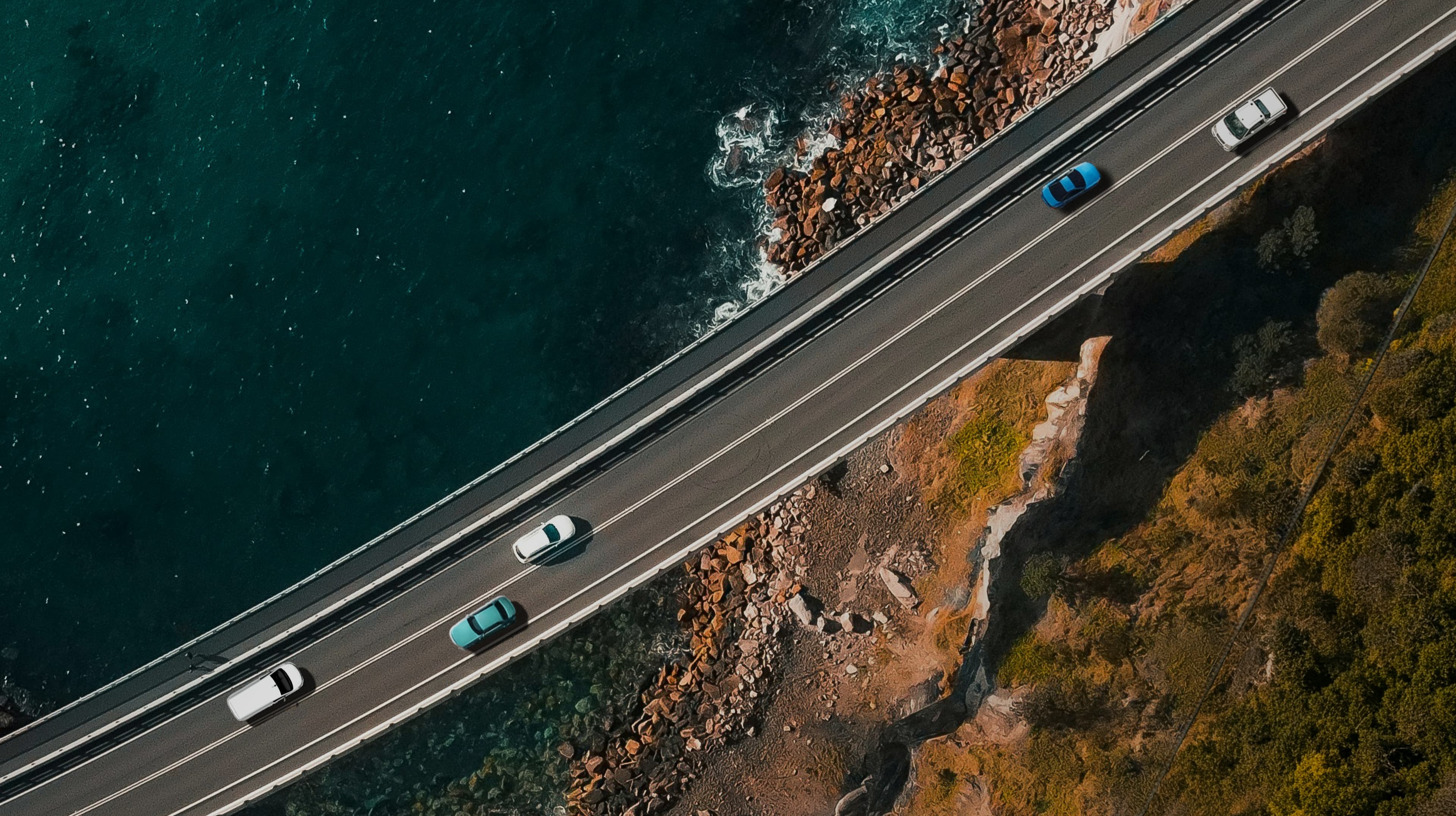 Aerial view of cars traveling along a coastal highway beside the ocean. Aerial view of cars traveling along a coastal highway beside the ocean.
