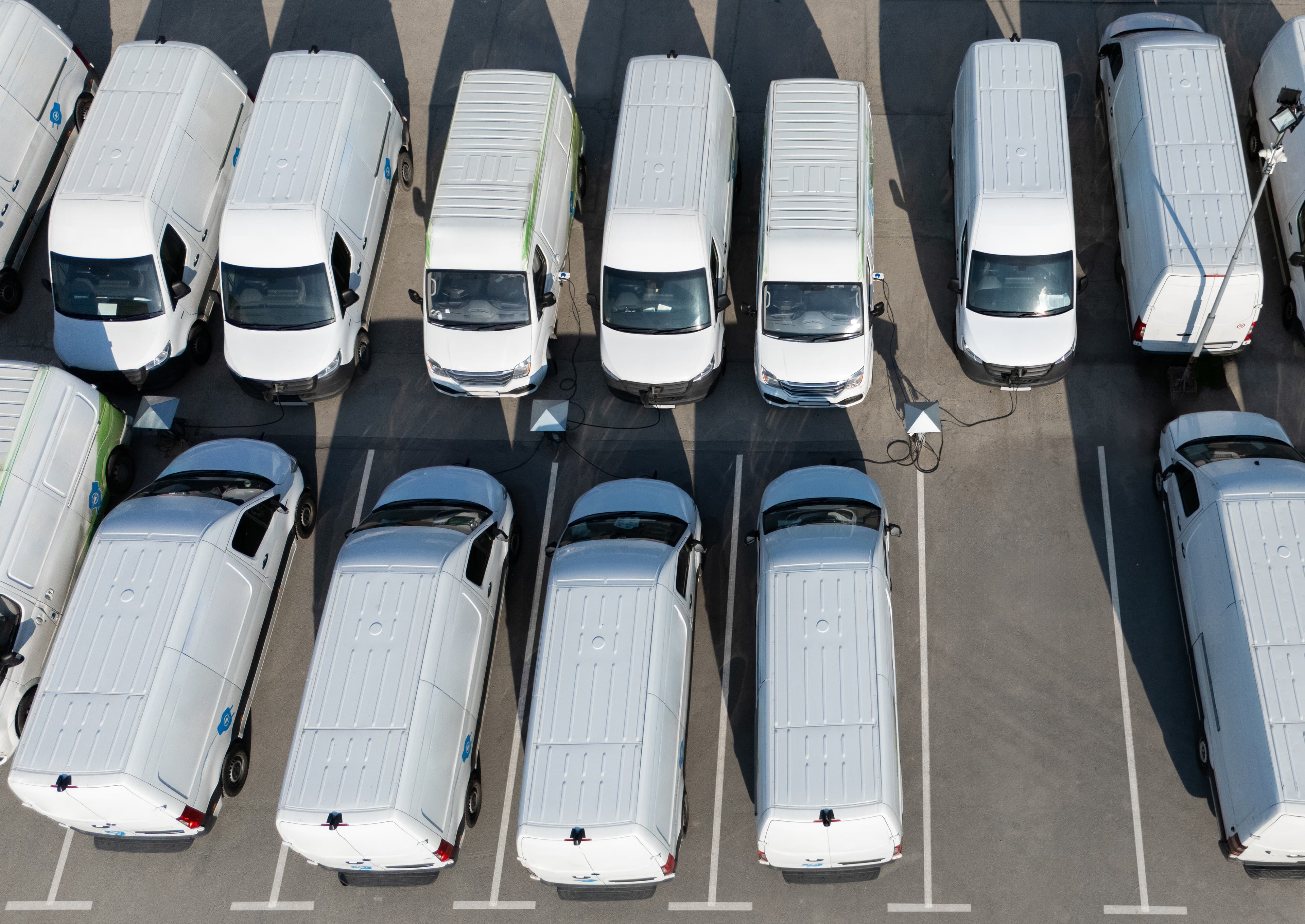 Fleet of white delivery vans parked in organized rows in a commercial parking lot, overhead aerial view. Fleet of white delivery vans parked in organized rows in a commercial parking lot, overhead aerial view.