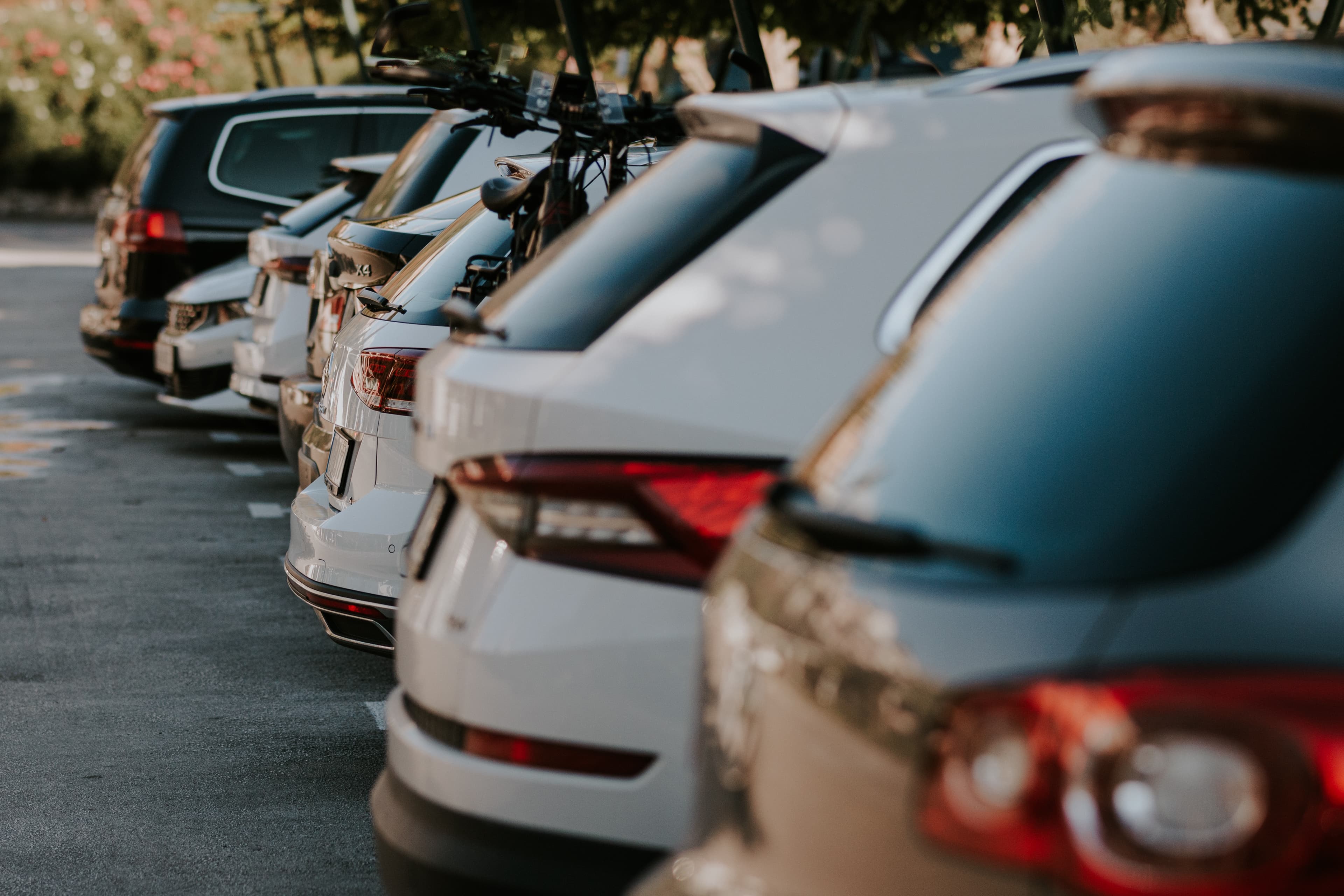 A row of parked vehicles in an outdoor parking lot, with several SUVs lined up closely together on a sunny day. A row of parked vehicles in an outdoor parking lot, with several SUVs lined up closely together on a sunny day.