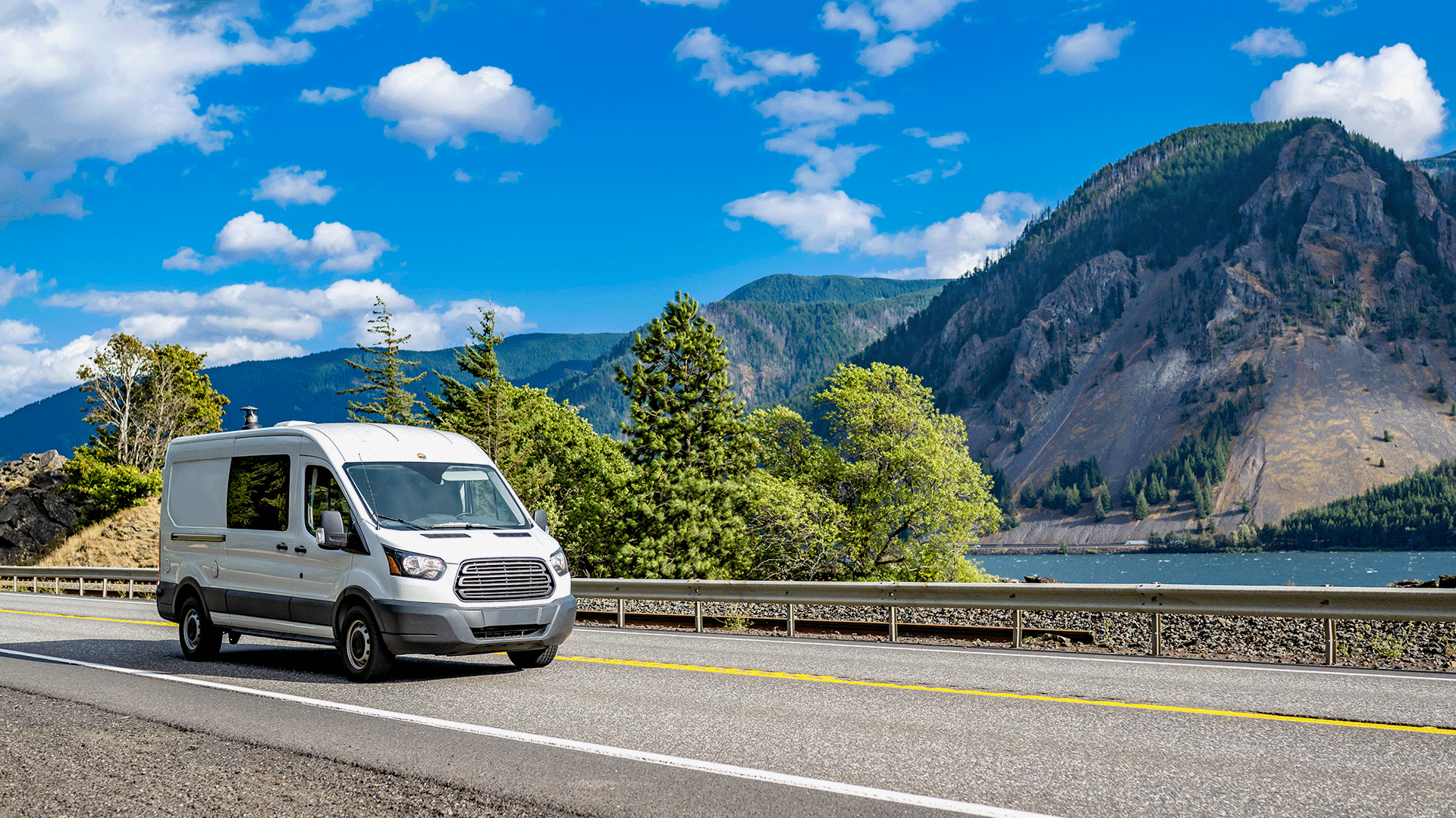 A delivery van driving along a scenic mountain road beside a lake. A delivery van driving along a scenic mountain road beside a lake.