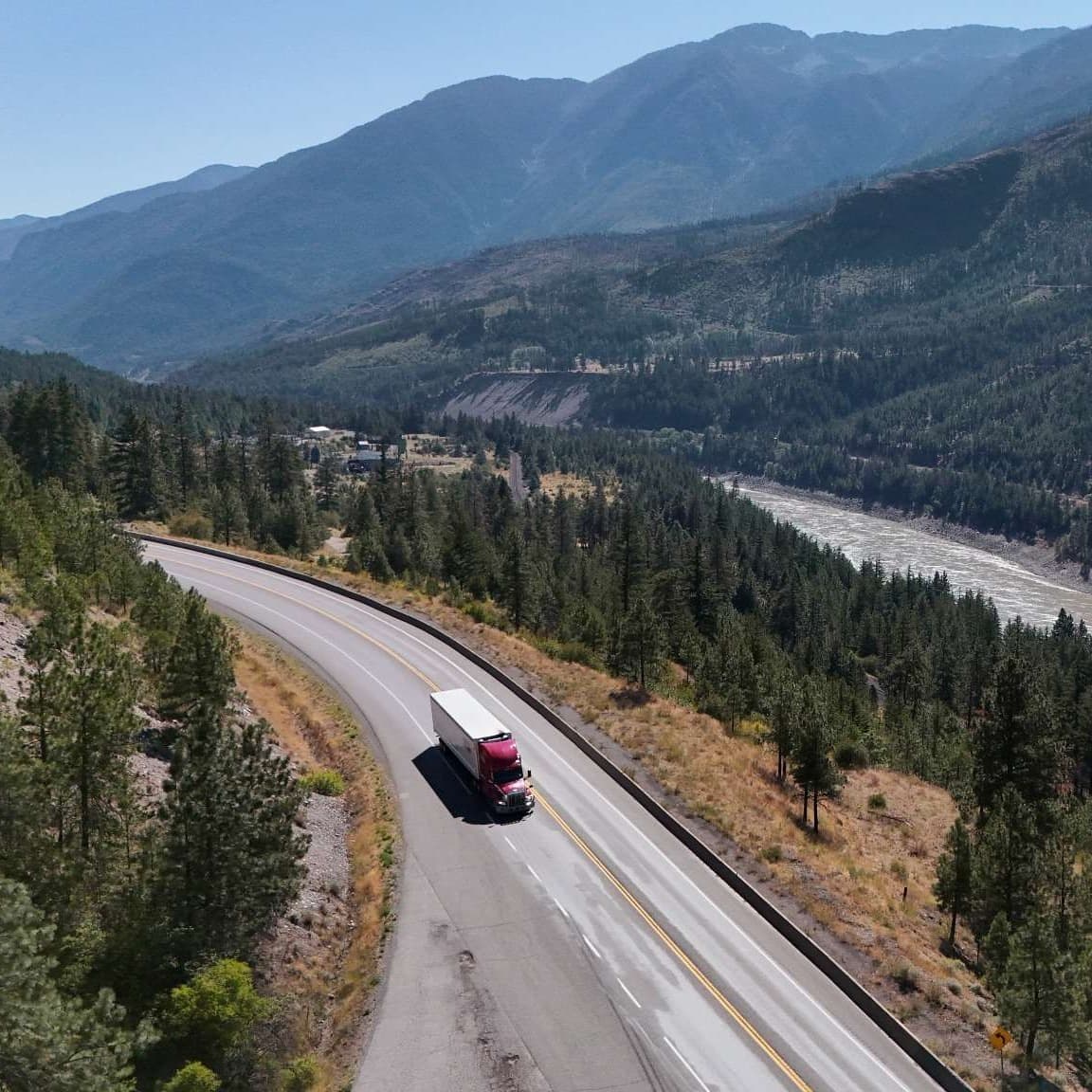 Red and white truck driving on a winding mountain highway surrounded by forest. Red and white truck driving on a winding mountain highway surrounded by forest.