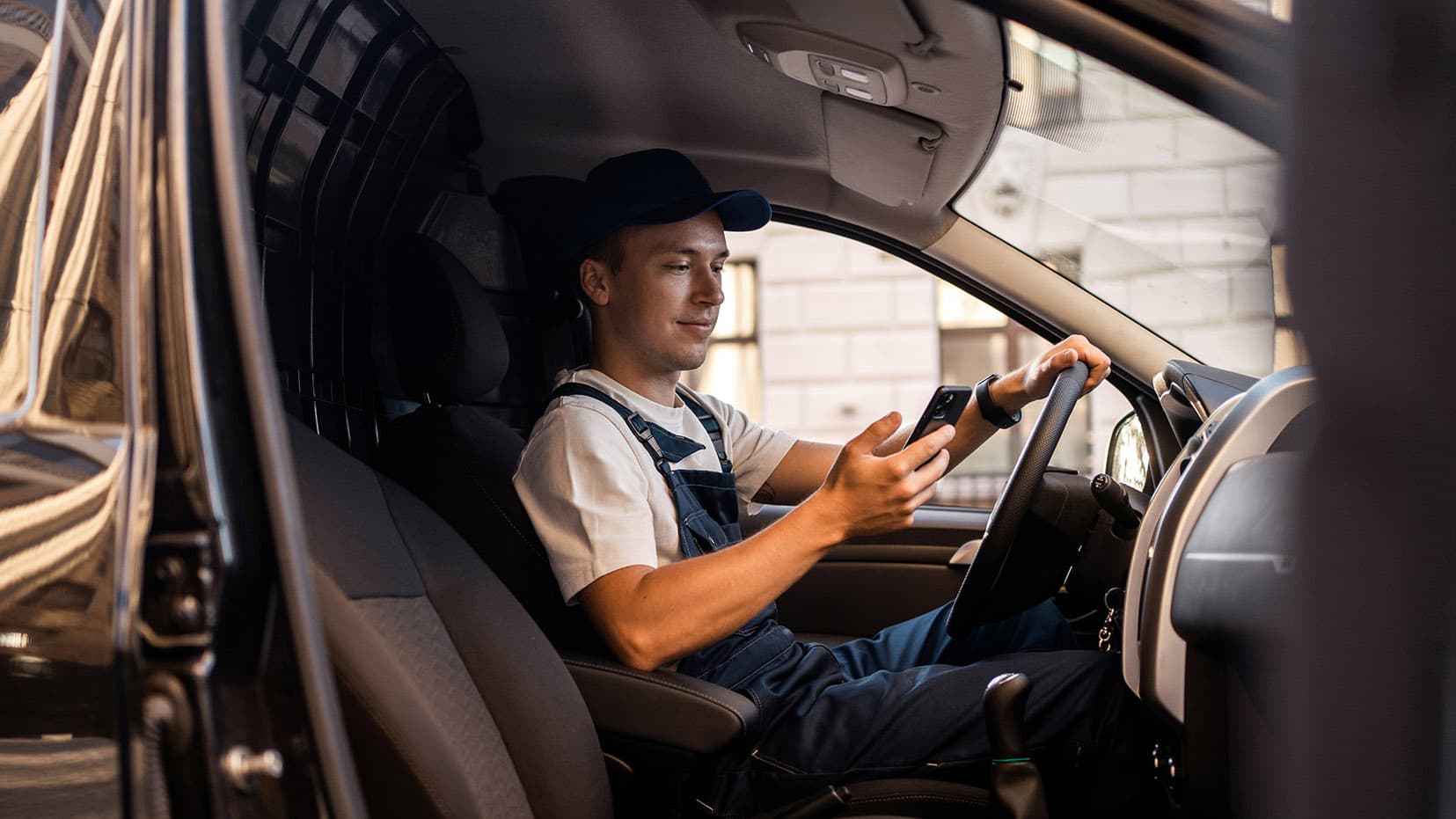 A delivery driver using a smartphone while sitting inside a delivery van. A delivery driver using a smartphone while sitting inside a delivery van.