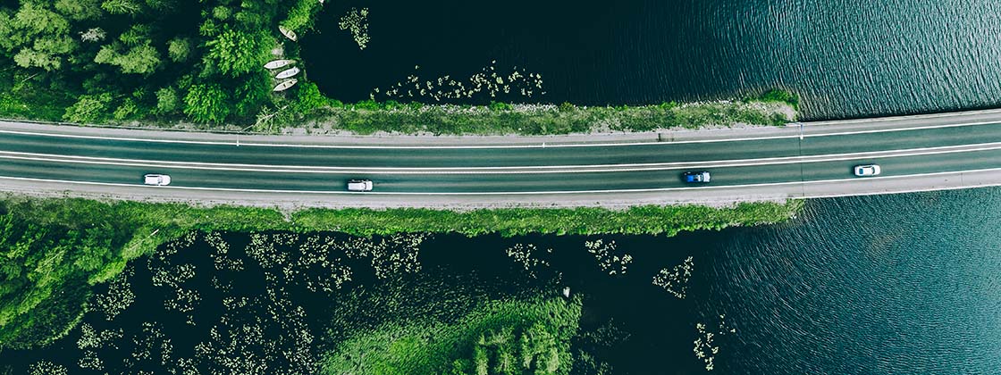A high overhead shot of vehicles driving along a road surrounded by greenery and water.