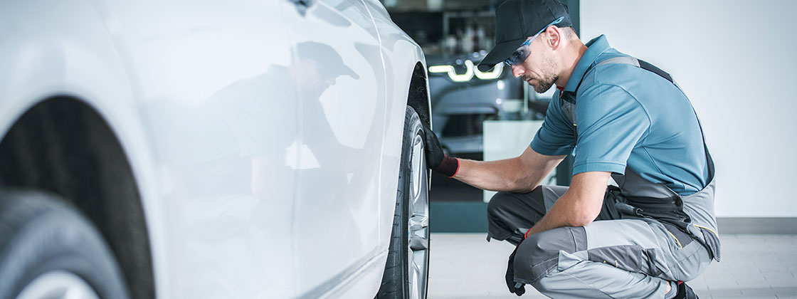 mechanic kneeling next to white car