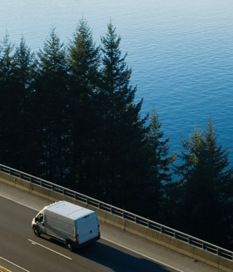 White van traveling on a road against a lake